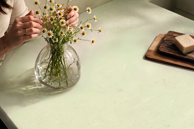 A person arranging small white flowers in a clear glass vase on a white surface.